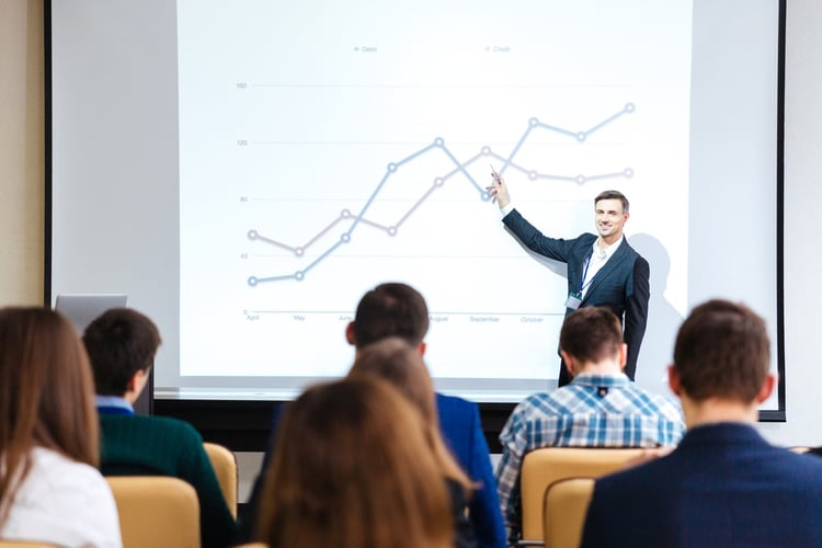 Smiling handsome speaker standing and explaining graphs on business conference in meeting hall.jpeg